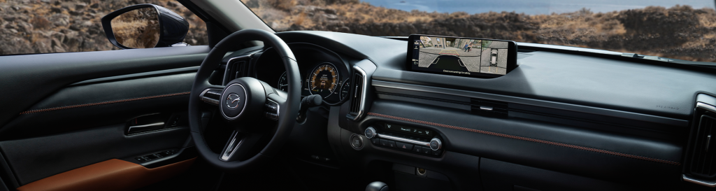 Interior view of a Mazda CX-50, featuring a sleek dashboard design with a multifunction steering wheel, digital display, and a rearview camera showing on the infotainment screen.