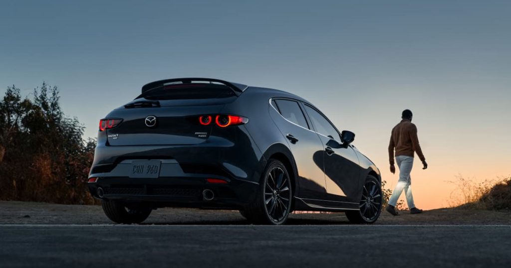 A black 2025 Mazda 3 hatchback parked off-road during sunset.
