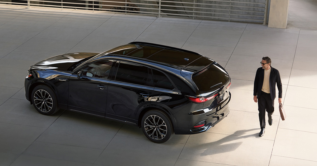 A man walking past a Mazda CX-70 in Jet Black Mica in a parking lot.