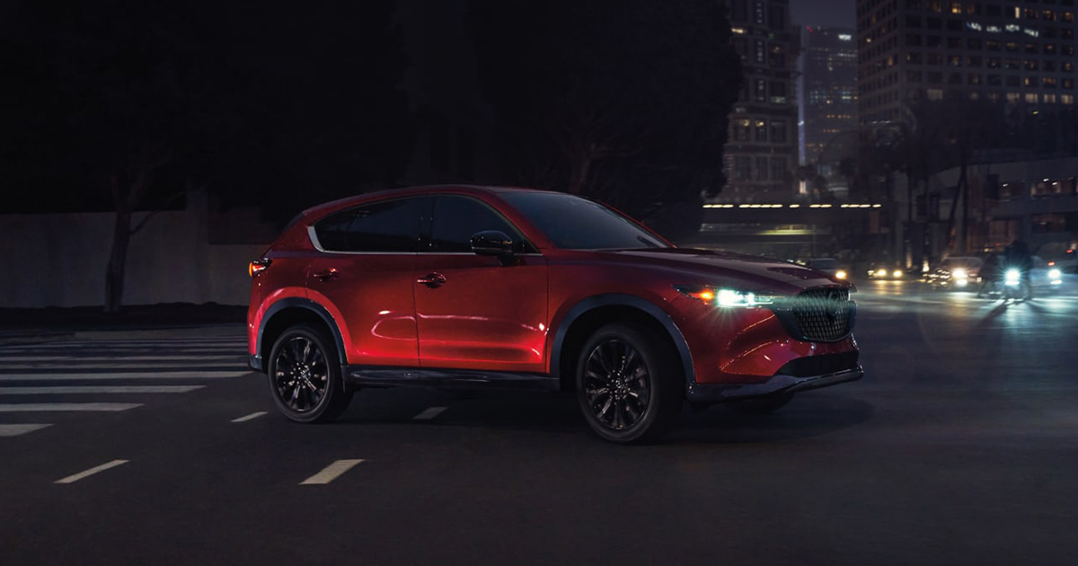 A red Mazda CX-5 driving through city streets at night.