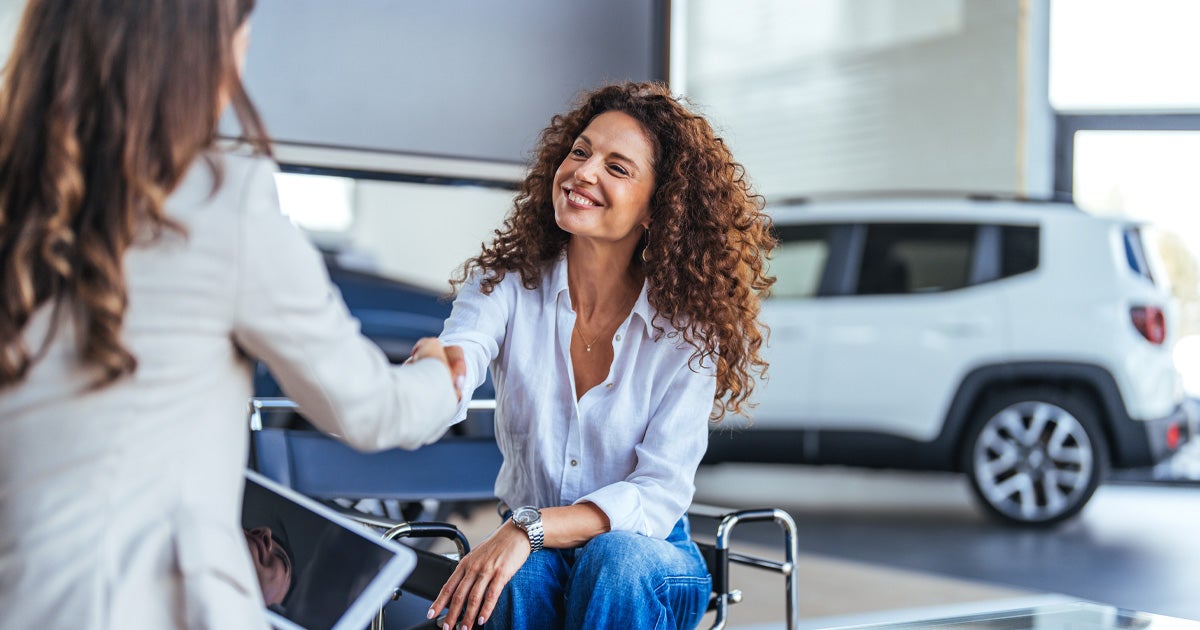 A smiling customer shaking hands with the car salesperson inside the dealership showroom.